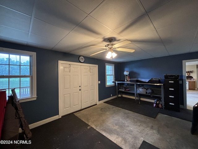 interior space with a paneled ceiling, ceiling fan, and concrete floors