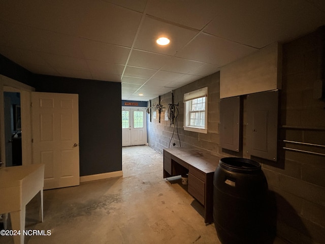 interior space with concrete block wall, electric panel, a drop ceiling, and unfinished concrete floors