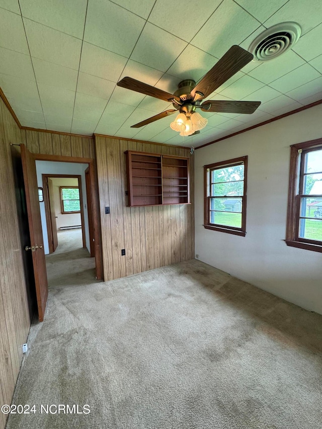 unfurnished bedroom featuring wooden walls, carpet floors, multiple windows, and ceiling fan