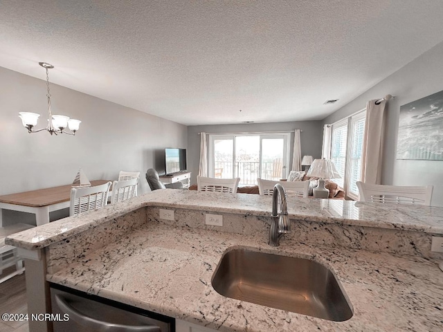 kitchen featuring sink, light stone countertops, a textured ceiling, and pendant lighting