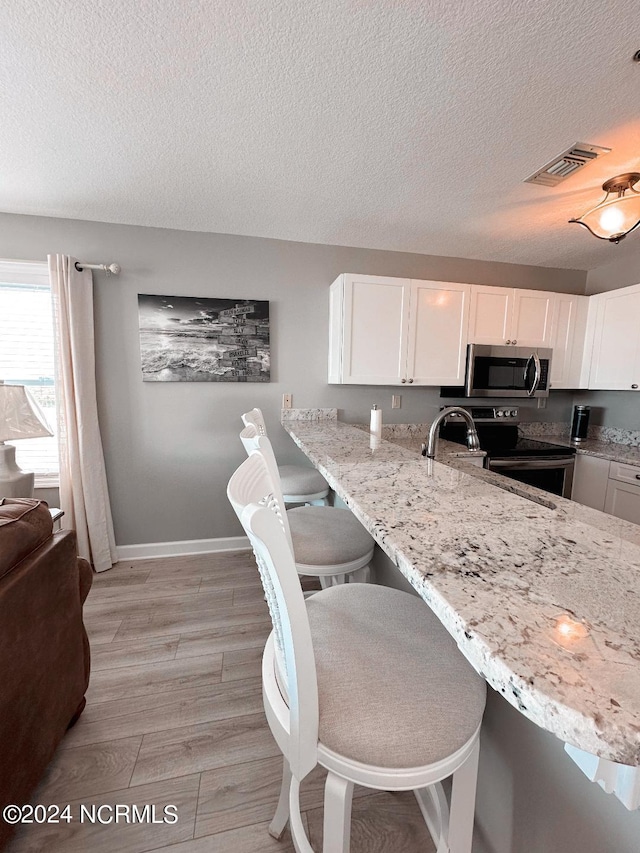 kitchen featuring light hardwood / wood-style floors, a textured ceiling, stainless steel appliances, white cabinets, and a kitchen bar