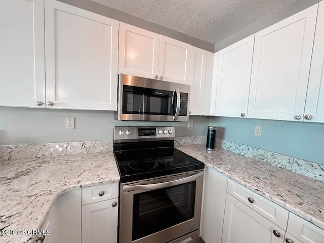 kitchen with appliances with stainless steel finishes, white cabinetry, a textured ceiling, and light stone countertops