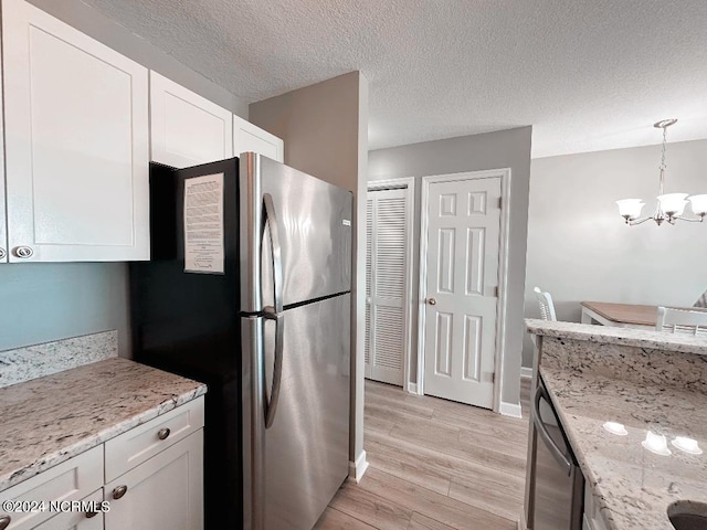 kitchen with stainless steel appliances, light wood-type flooring, light stone counters, hanging light fixtures, and white cabinets