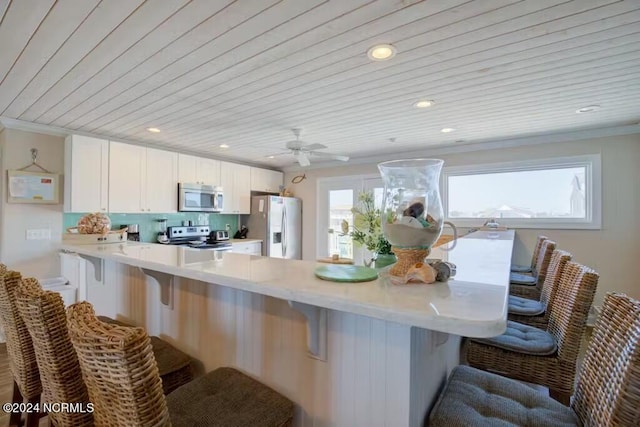 kitchen featuring white cabinets, ceiling fan, tasteful backsplash, a breakfast bar area, and appliances with stainless steel finishes