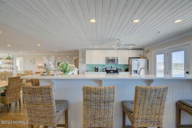 kitchen featuring light hardwood / wood-style floors, wood ceiling, white cabinets, a breakfast bar, and appliances with stainless steel finishes