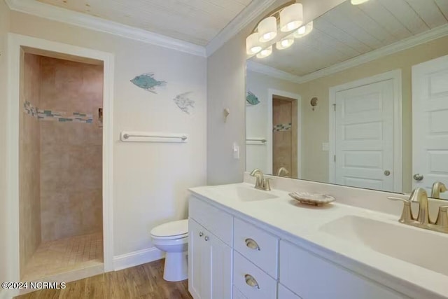 bathroom with tiled shower, ornamental molding, double sink vanity, wood-type flooring, and toilet