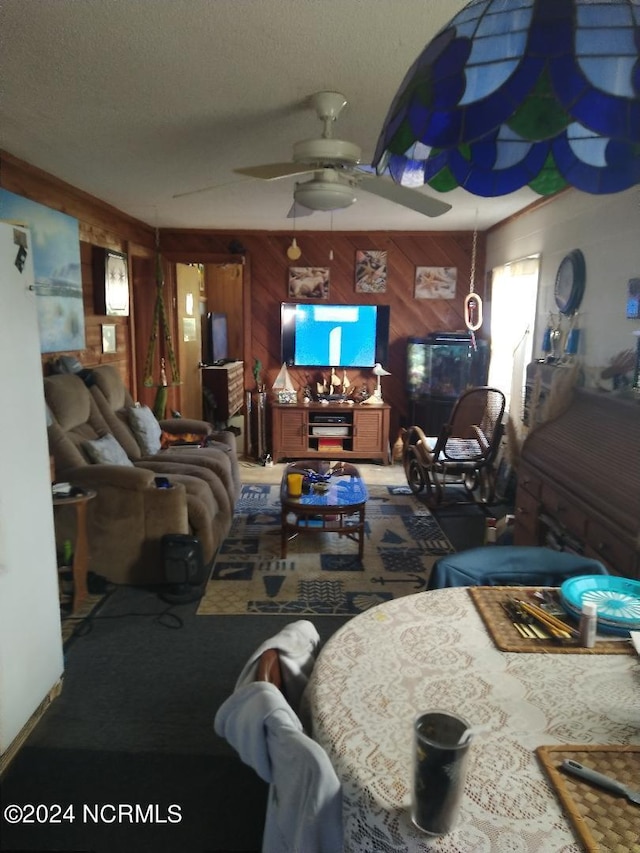 carpeted living room with a textured ceiling, ceiling fan, and wood walls