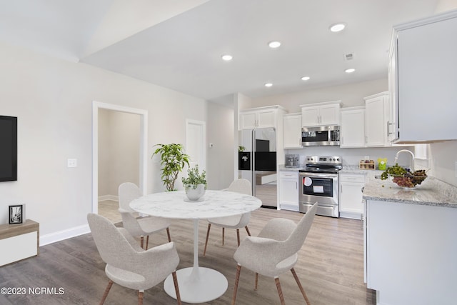 kitchen with hardwood / wood-style flooring, appliances with stainless steel finishes, light stone counters, and white cabinets