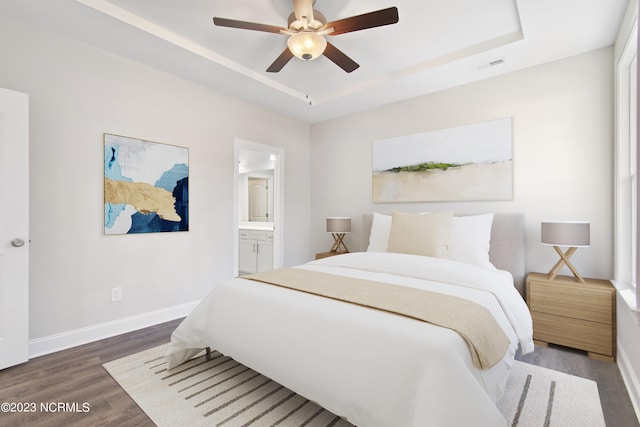 bedroom with ceiling fan, ensuite bath, a raised ceiling, and dark wood-type flooring