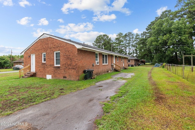 view of side of property with entry steps, a lawn, crawl space, fence, and brick siding