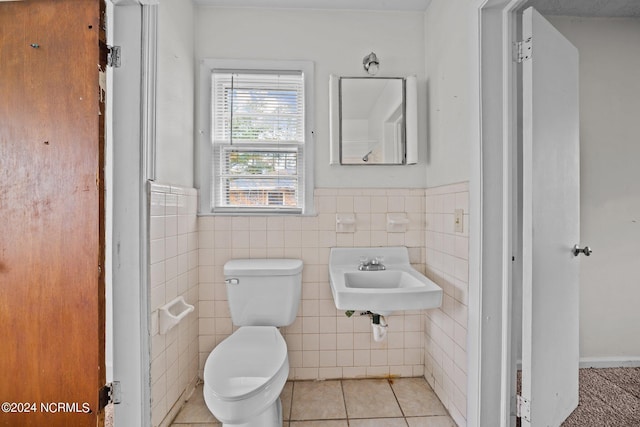 half bathroom with toilet, a sink, tile walls, wainscoting, and tile patterned floors