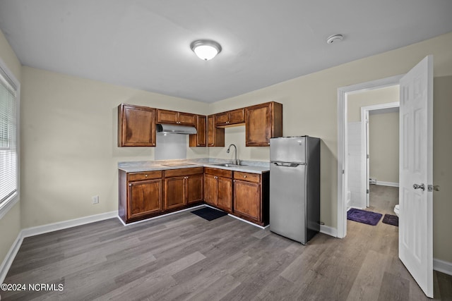 kitchen featuring under cabinet range hood, a sink, light countertops, freestanding refrigerator, and brown cabinets