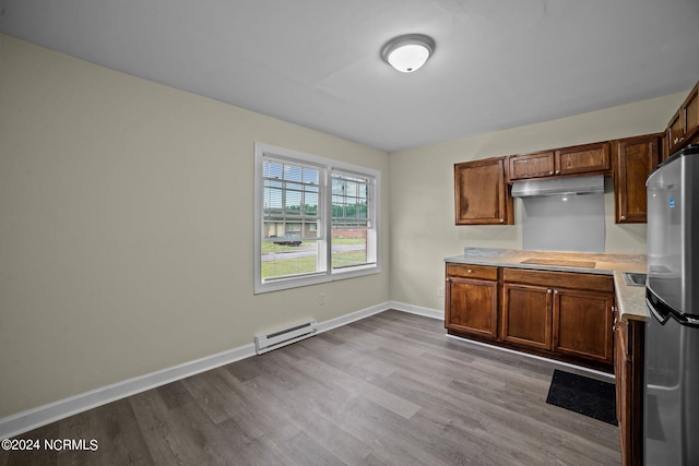 kitchen featuring brown cabinets, light countertops, a baseboard heating unit, freestanding refrigerator, and under cabinet range hood