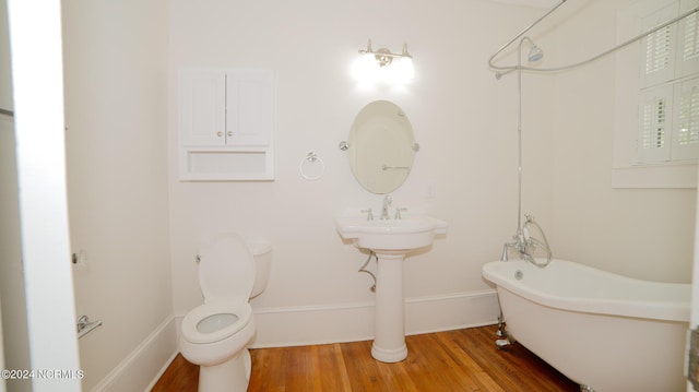 full bath featuring baseboards, a freestanding bath, toilet, and wood finished floors