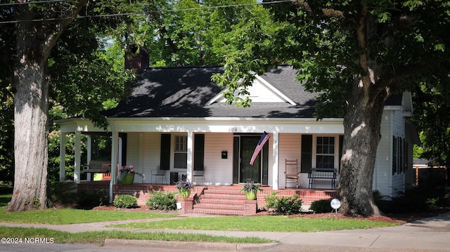 view of front facade with a shingled roof, a chimney, and a porch