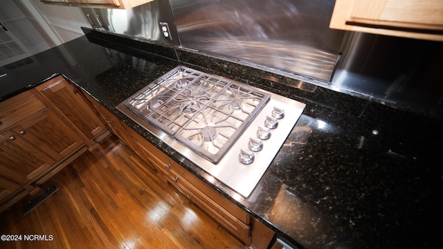 details with visible vents, dark stone counters, brown cabinets, dark wood-style flooring, and stainless steel gas cooktop