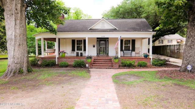 view of front of home with covered porch, a shingled roof, and fence