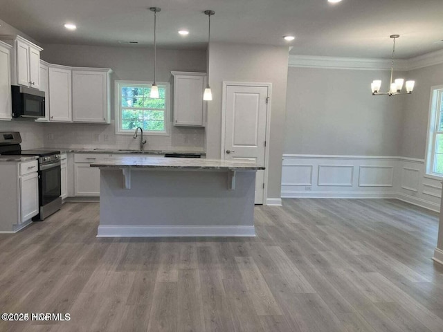 kitchen with appliances with stainless steel finishes, a center island, white cabinets, and decorative light fixtures