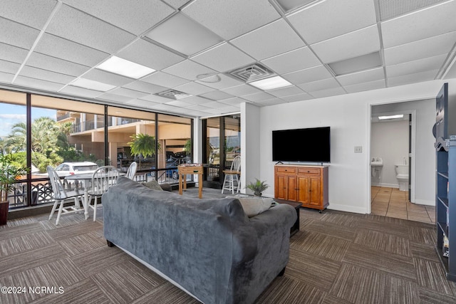 living room with dark carpet, a wall of windows, and a drop ceiling