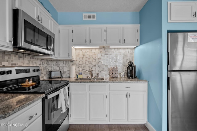 kitchen with stainless steel appliances, backsplash, sink, white cabinets, and hardwood / wood-style flooring