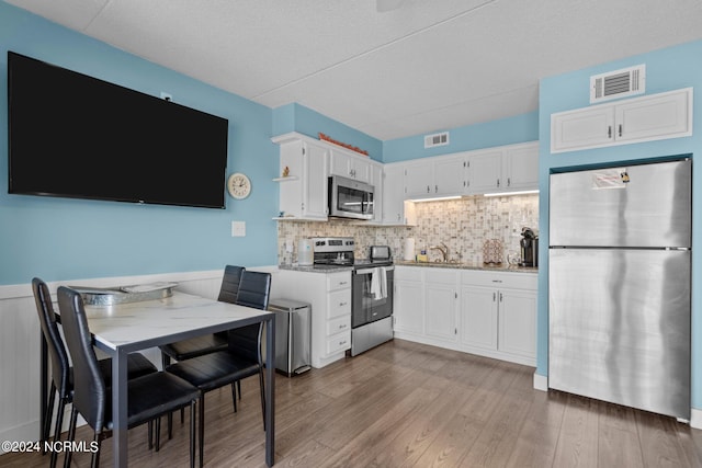 kitchen featuring stainless steel appliances, wood-type flooring, light stone counters, backsplash, and white cabinetry