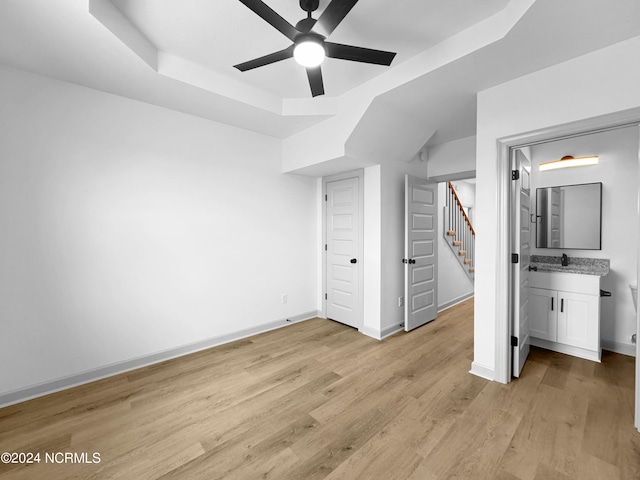 unfurnished bedroom with a tray ceiling, light wood-style floors, a sink, ceiling fan, and baseboards