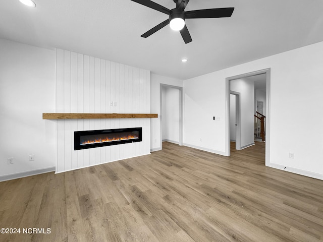 unfurnished living room featuring a large fireplace, ceiling fan, baseboards, and wood finished floors