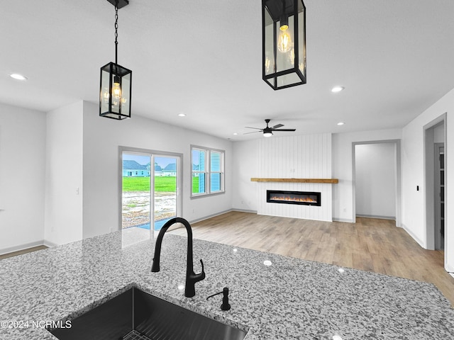 kitchen with wood finished floors, light stone countertops, a fireplace, a sink, and recessed lighting