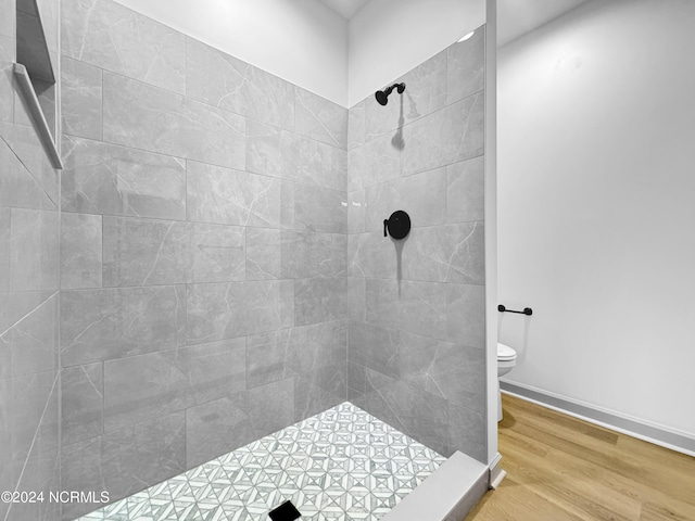 full bathroom featuring toilet, baseboards, tiled shower, and wood finished floors