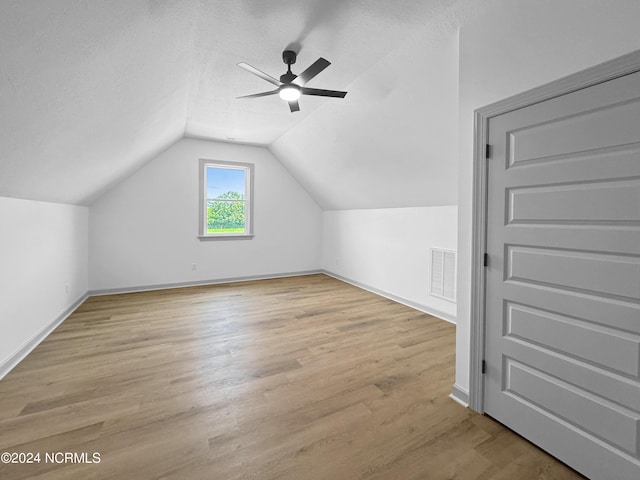 bonus room with a textured ceiling, lofted ceiling, wood finished floors, visible vents, and baseboards