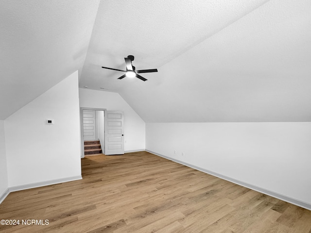 bonus room featuring light wood-style floors, lofted ceiling, ceiling fan, and a textured ceiling