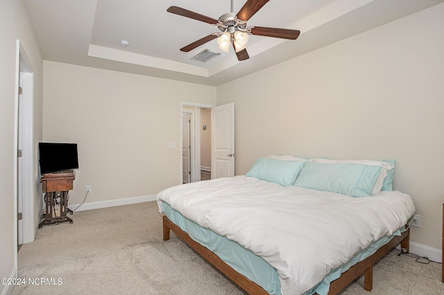 bedroom with a raised ceiling, light colored carpet, visible vents, ceiling fan, and baseboards