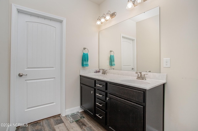 bathroom with double vanity, wood finished floors, a sink, and baseboards