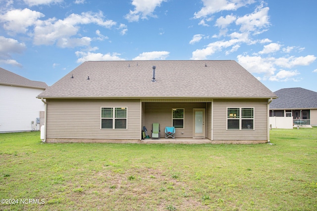 back of house with roof with shingles, a lawn, and a patio area