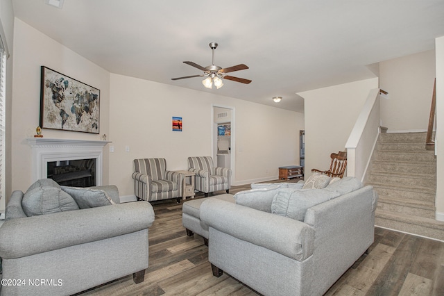 living area featuring stairs, a fireplace, wood finished floors, and a ceiling fan