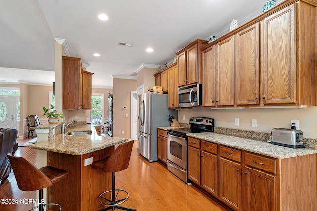 kitchen featuring kitchen peninsula, appliances with stainless steel finishes, light wood-type flooring, a kitchen breakfast bar, and sink