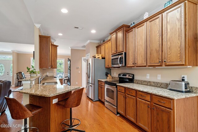 227 October Glory Dr, Wallace, NC 28466 - kitchen with stainless steel appliances, a sink, a breakfast bar, ornamental molding, and light wood-style flooring