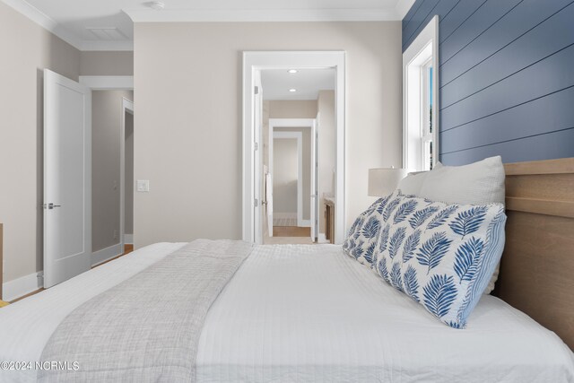 bedroom featuring connected bathroom, ornamental molding, and wood walls