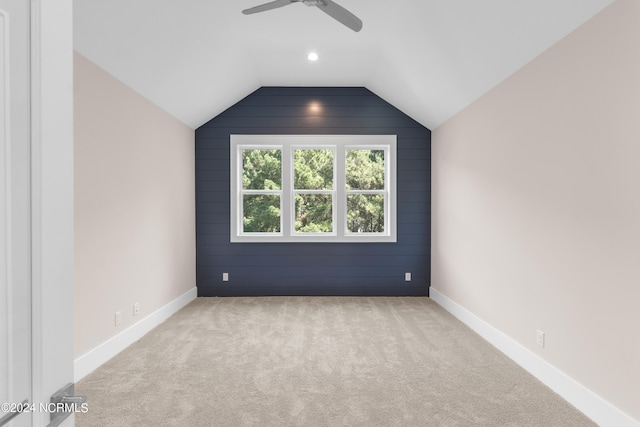 interior space with light carpet, wooden walls, ceiling fan, and vaulted ceiling