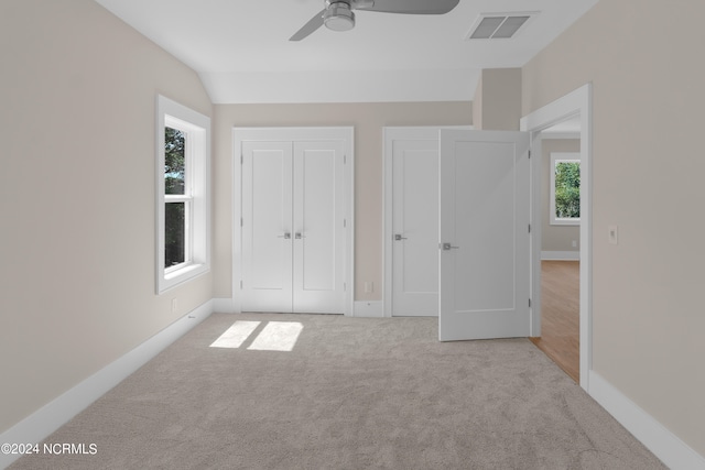 unfurnished bedroom featuring light carpet, vaulted ceiling, multiple windows, and ceiling fan