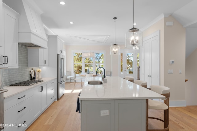 kitchen with a kitchen island with sink, hanging light fixtures, stainless steel appliances, and light hardwood / wood-style floors