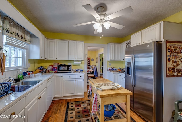 kitchen featuring tile counters, appliances with stainless steel finishes, white cabinets, a sink, and wood finished floors