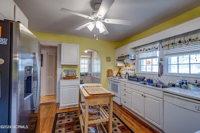 kitchen featuring arched walkways, light wood-style flooring, white cabinets, a sink, and white appliances