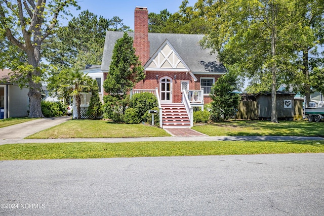 tudor home featuring a front yard, brick siding, a chimney, and roof with shingles