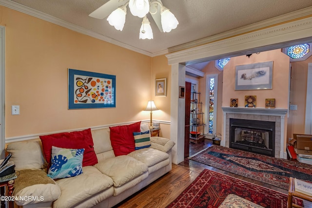 living area featuring wood finished floors, ornamental molding, a textured ceiling, and a tile fireplace