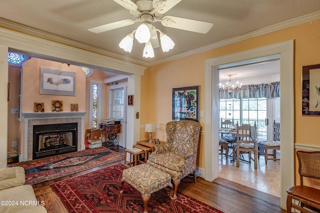 living area with a fireplace, ornamental molding, a textured ceiling, and wood finished floors