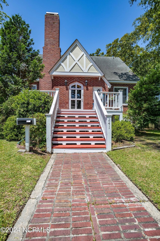 english style home featuring brick siding, a chimney, stairway, and a front yard