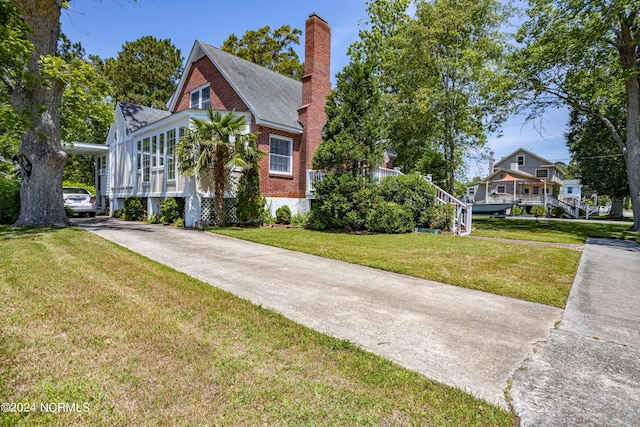 view of front facade featuring concrete driveway, brick siding, a chimney, and a front yard