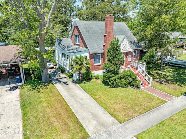 view of front facade featuring brick siding, driveway, a chimney, and a front lawn