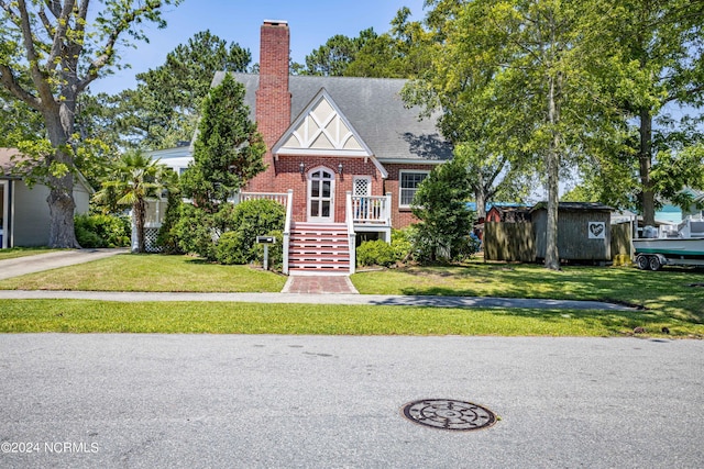 tudor-style house with a shingled roof, a chimney, stairway, a front lawn, and brick siding